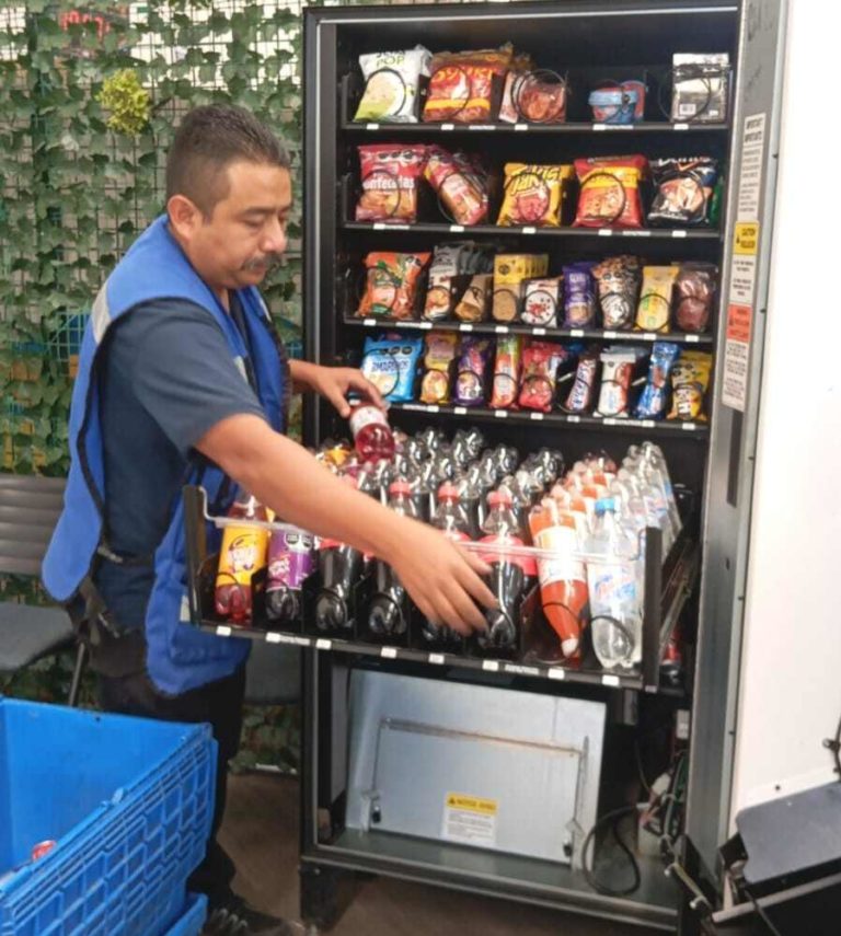 Vending service technician restocking and maintaining a modern drinks vending machine in a workplace.