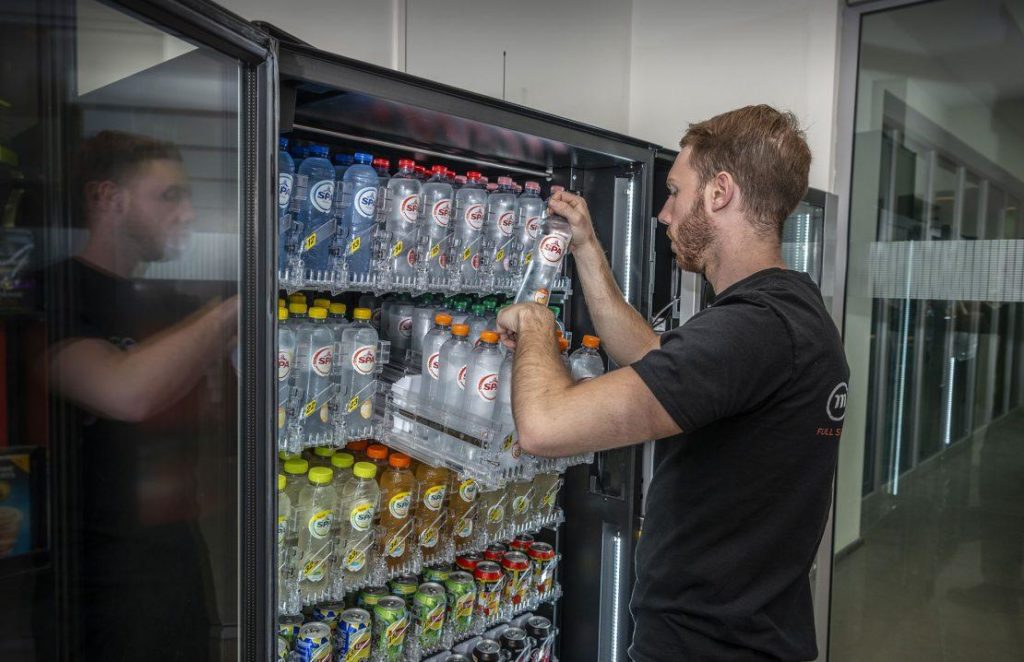 Vending service technician restocking a modern snack and drinks vending machine in a commercial workplace.
