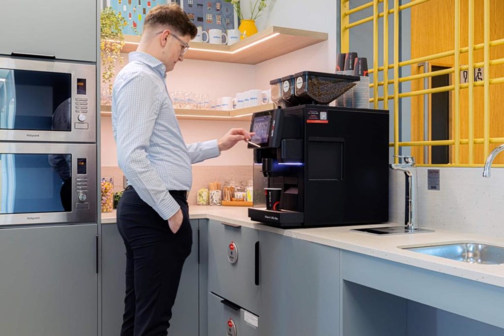 Employee using a touchscreen bean-to-cup coffee machine in a modern office break room.